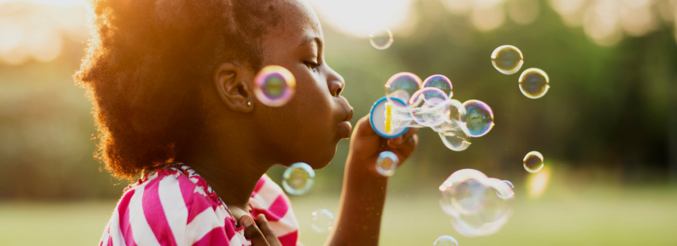 African descent girl playing blowing bubble in a park